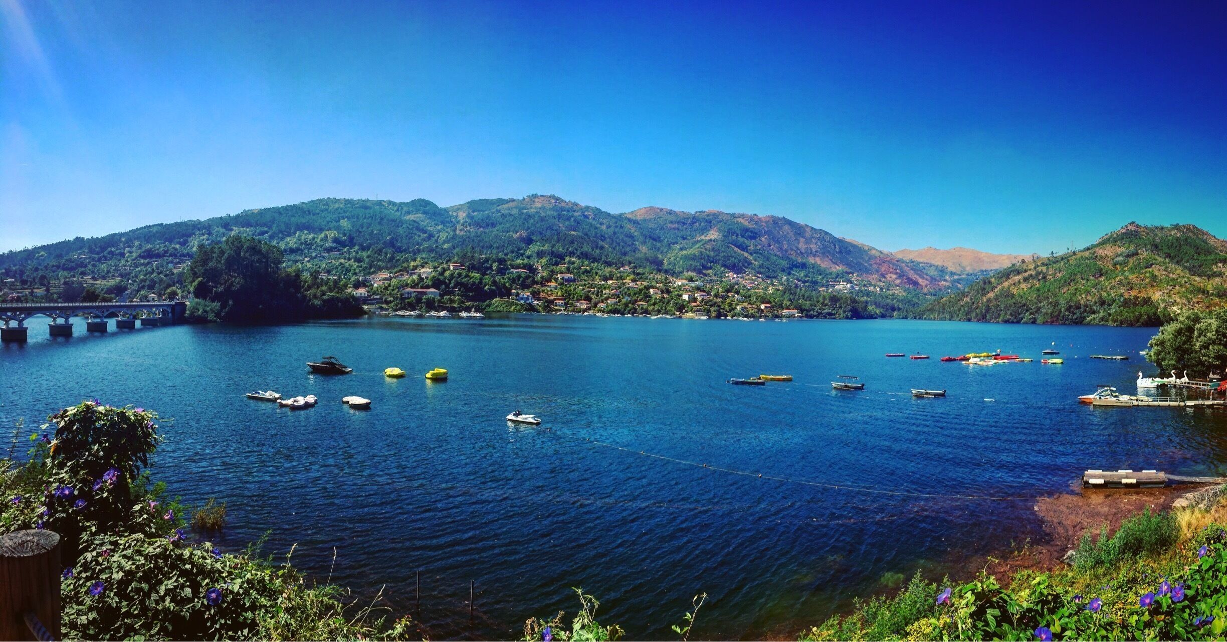 A calm lake with boats, a bridge, and mountains in the background.