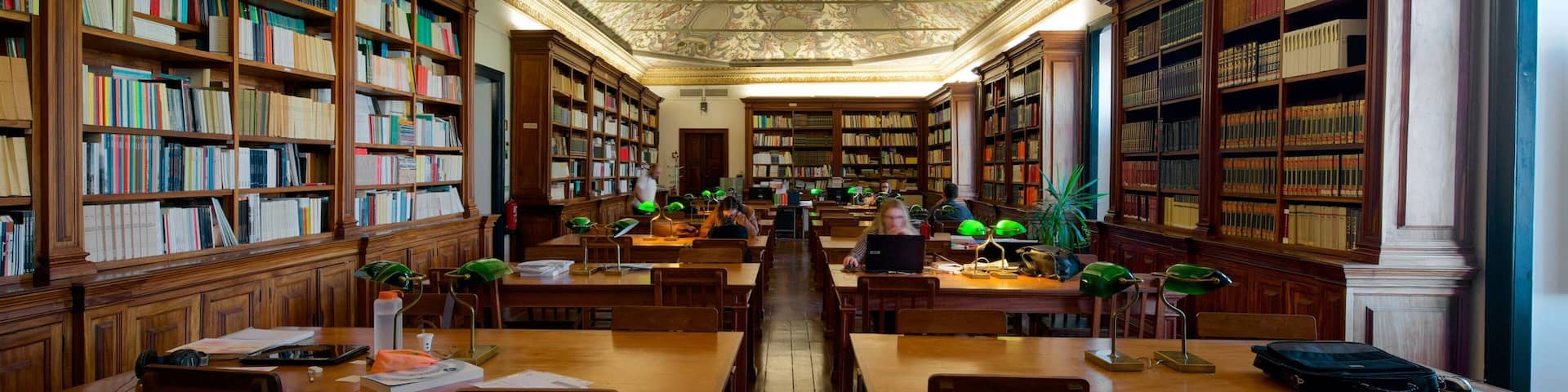 A library with ornate ceilings, wooden bookshelves, and study tables.