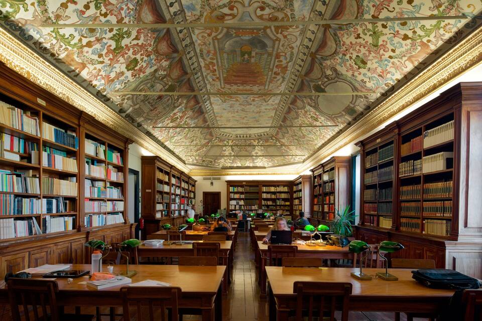 Een bibliotheek met versierde plafonds, houten boekenkasten en studeertafels.