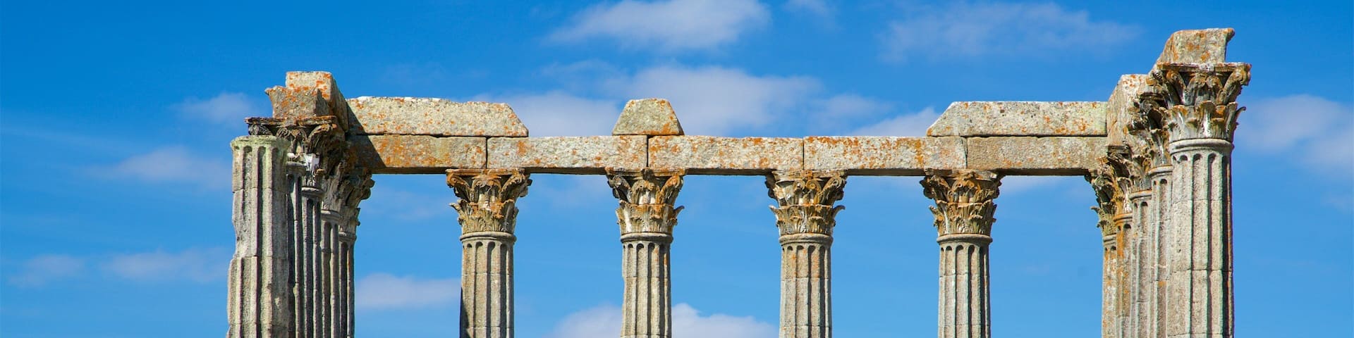 Ancient stone columns with intricate capitals, set against a clear blue sky.