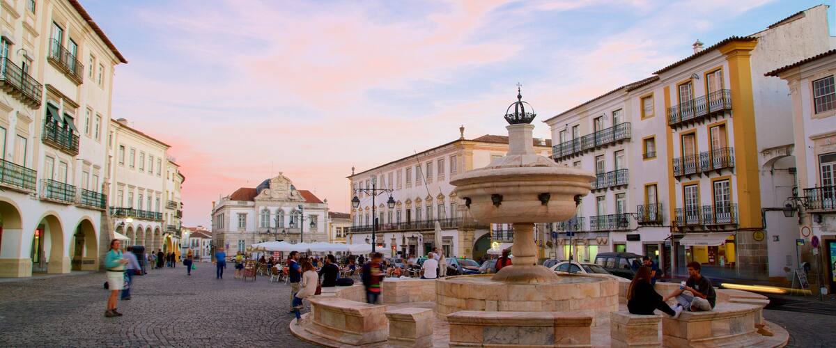 A cobblestone square with a central fountain, surrounded by historic buildings with balconies and arches.
