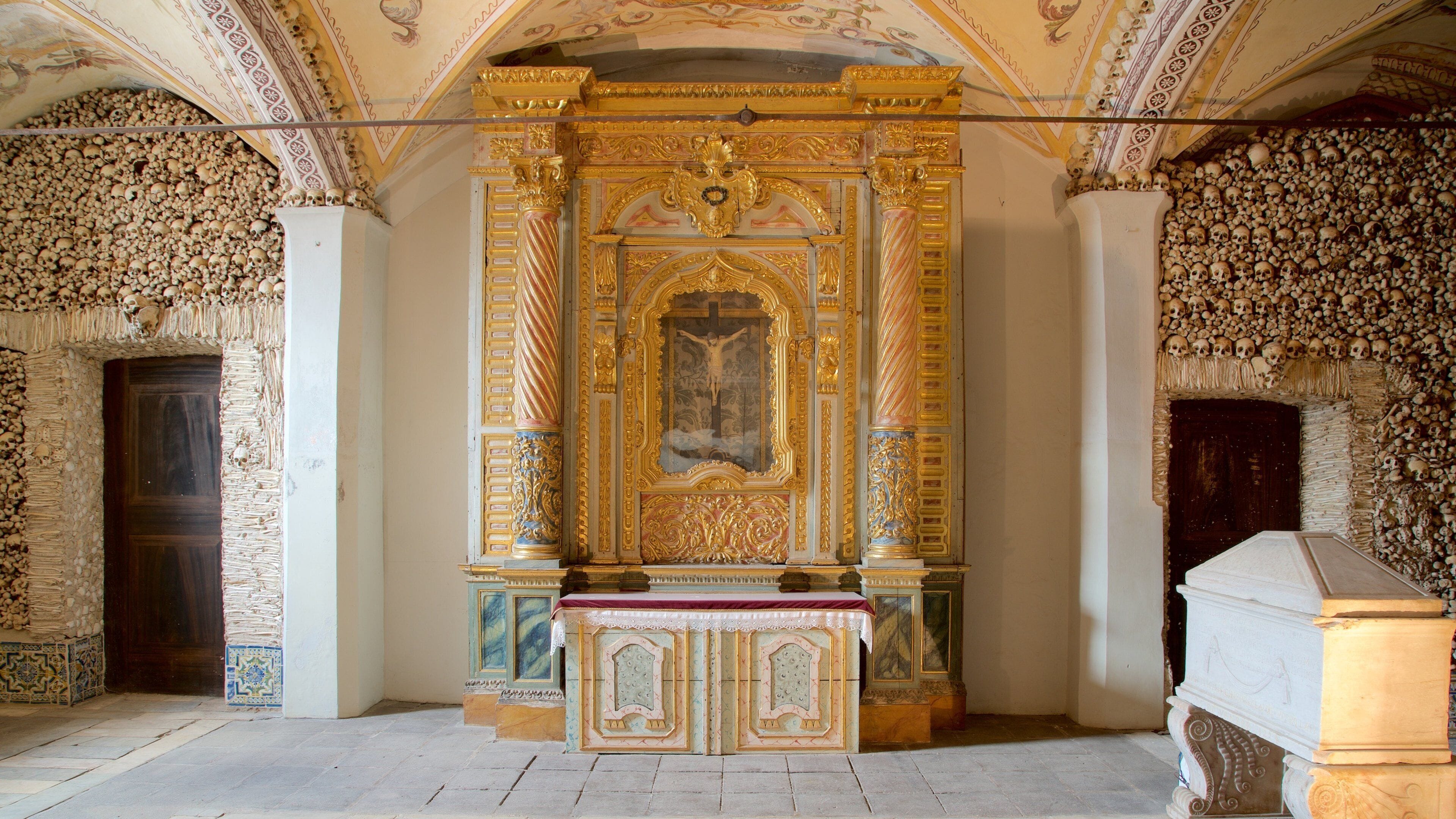 L’intérieur d’une chapelle richement décorée, avec un crucifix, des ornements dorés et des murs ornés de motifs représentant des crânes.