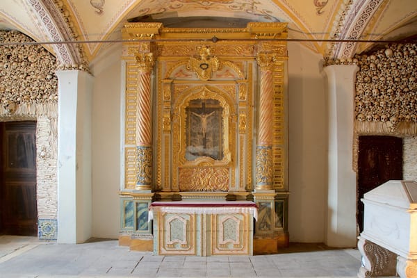 An ornate chapel interior with a crucifix, golden decorations, and skull-adorned walls.