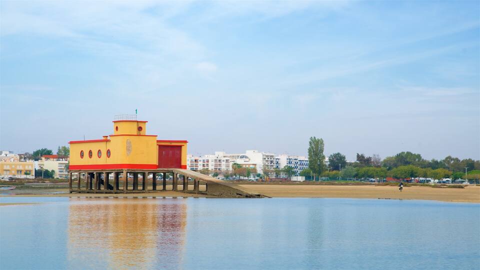 A yellow and red pier extending into a calm body of water with a cityscape in the background.