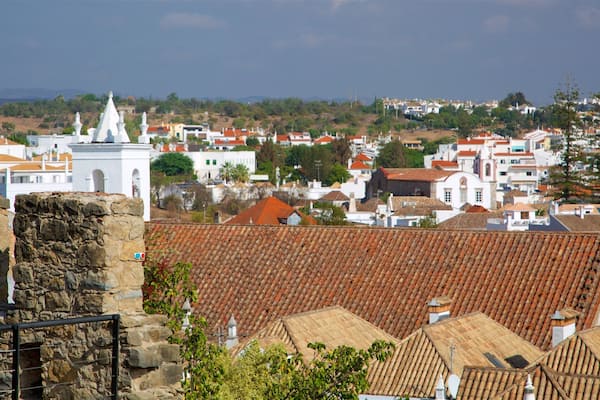 A coastal town with terracotta-roofed buildings, a prominent white church with a dome, and a stone wall in the foreground.