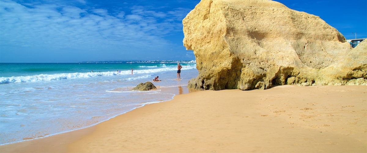 A sandy beach with a large rock formation and the ocean in the background.