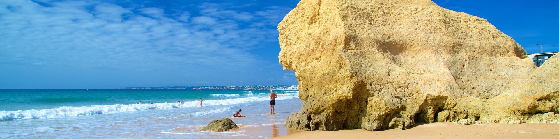 A sandy beach with a large rock formation and the ocean in the background.
