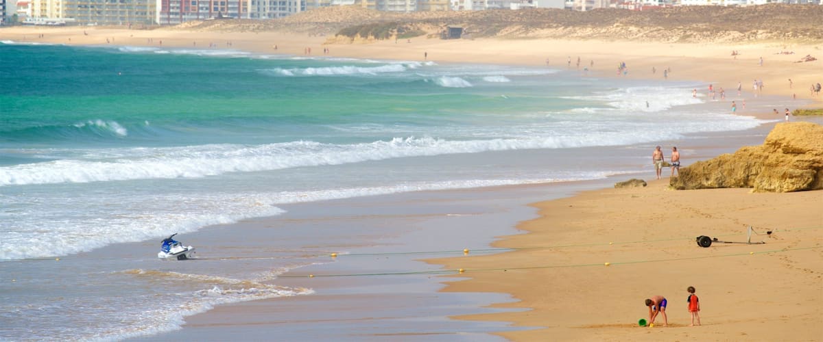 A beach with waves, a jet ski, and a cityscape in the background.