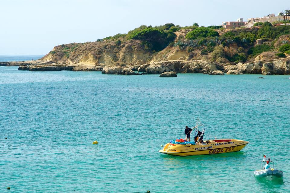 A coastal scene with a boat named 'PORTIMÃO' and 'COOL FLY' on turquoise water, rocky cliffs, and buildings in the background.