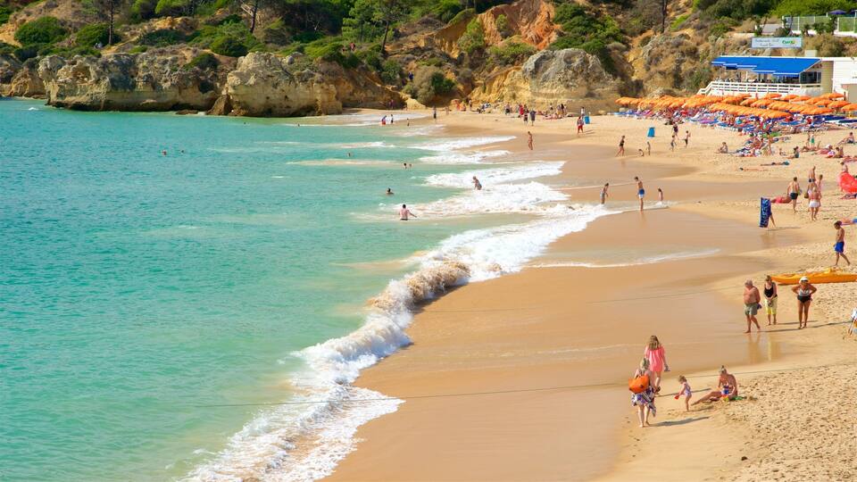A crowded beach with clear turquoise water, rocky cliffs, and umbrellas.