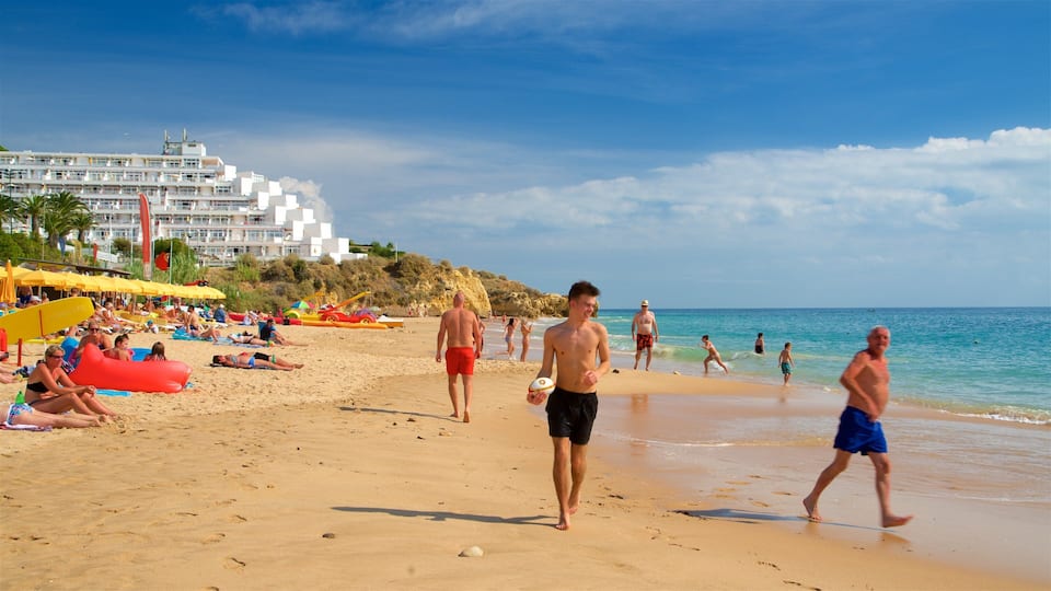 A sandy beach with people sunbathing, walking, and playing. There are umbrellas, beach chairs, and a building in the background.