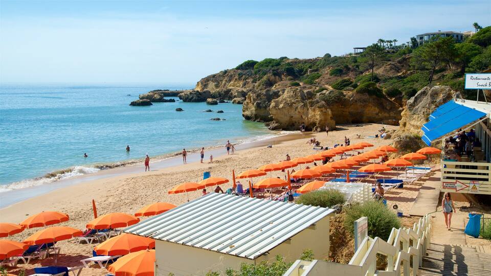A beach with orange umbrellas, people sunbathing, and a rocky cliff in the background.