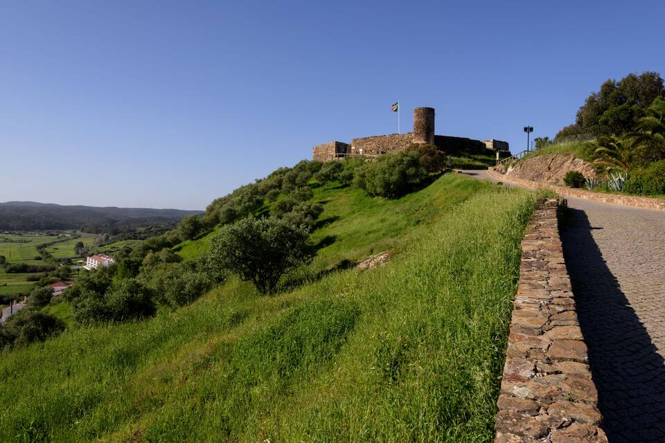 Uma fortaleza de pedra histórica numa colina com grama e céu limpo.