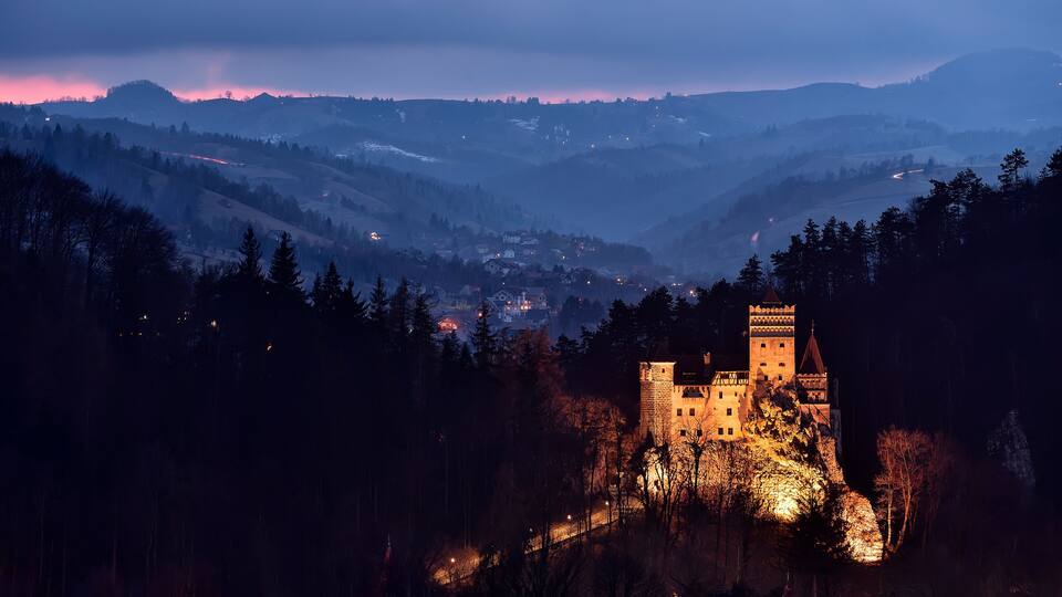 A castle on a hill, surrounded by forested hills and a valley.