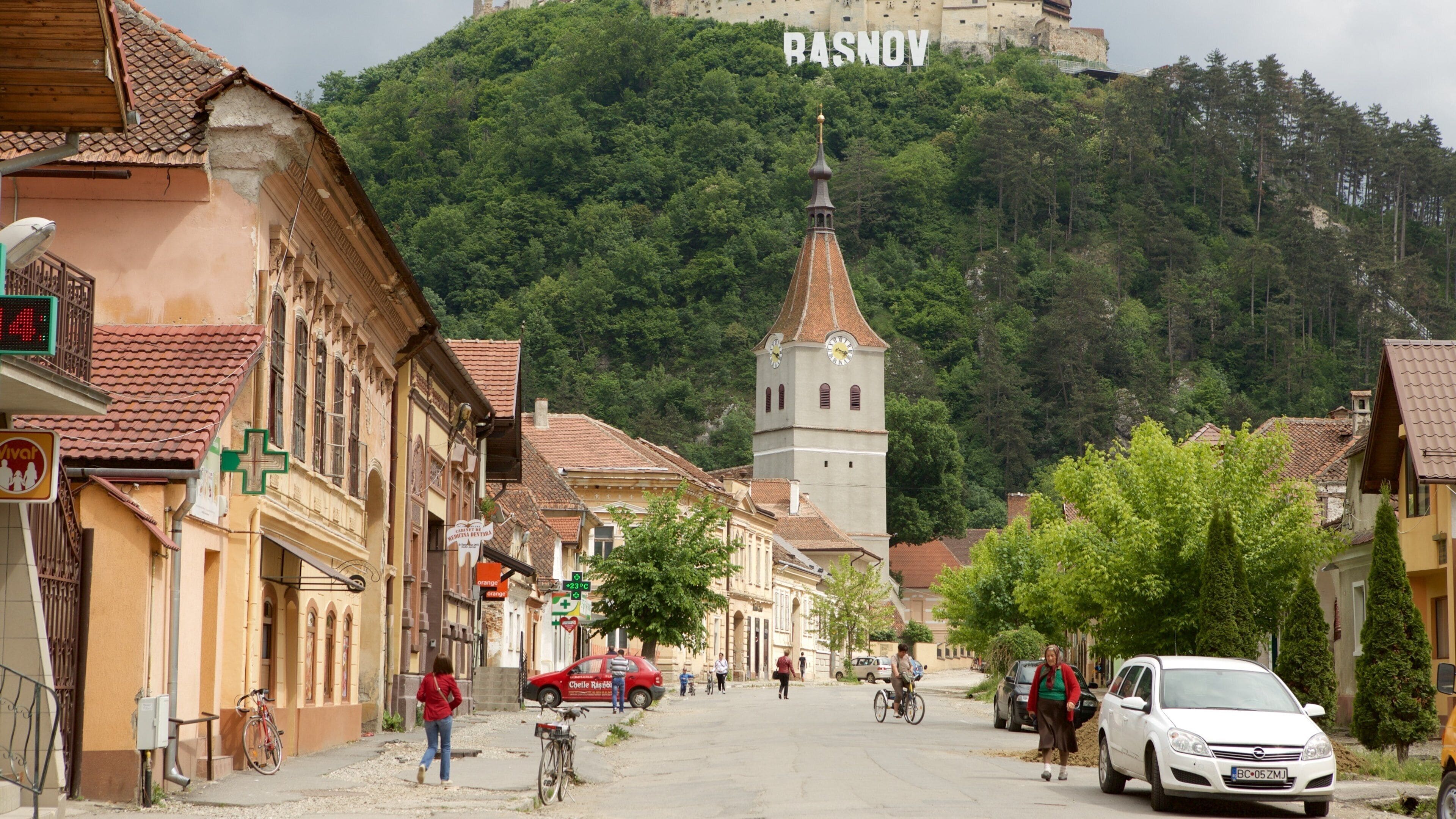 A town street with historic buildings, a clock tower, and a castle in the background.