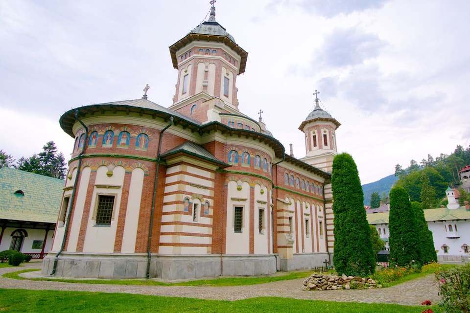 A historic church with two domes and a bell tower, surrounded by a well-maintained garden and a cobblestone path.