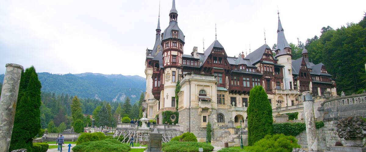 A historic castle with multiple spires, surrounded by lush greenery and a well-maintained garden.