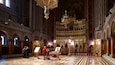 An ornate church interior with a central altar, multiple chandeliers, and intricate wall decorations.