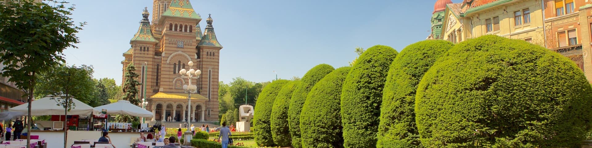 A historic church with a green spire, a café with outdoor seating, and neatly trimmed hedges.