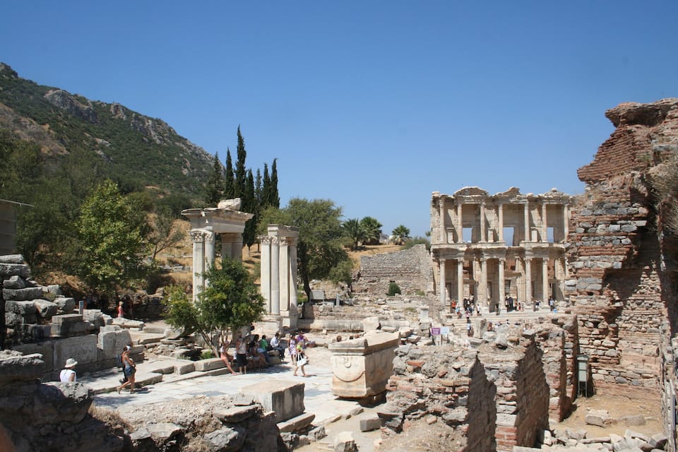 Vestiges antiques, avec des colonnes et des structures en pierre, entourés d’arbres et de collines.