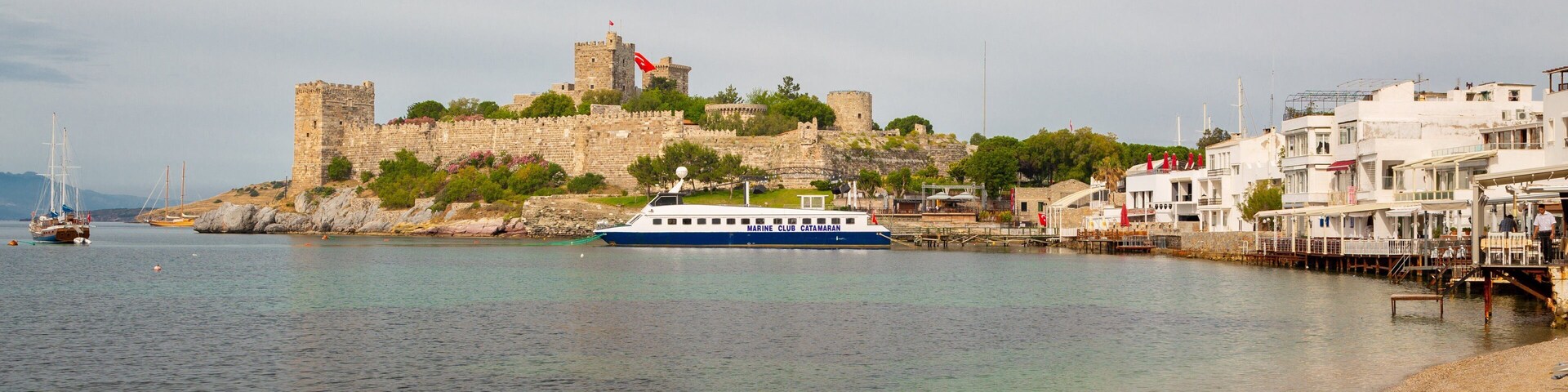Un pueblo costero con un castillo histórico, un puerto deportivo y una playa.