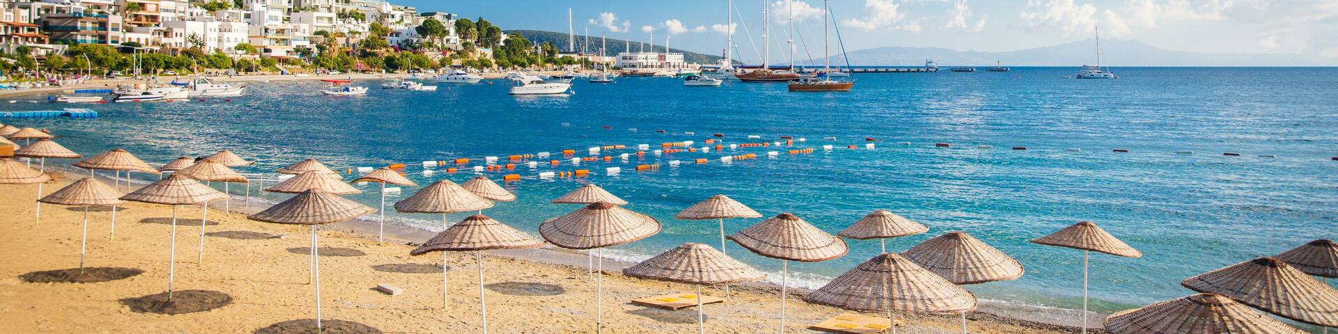 A beach with umbrellas, boats, and a coastal town.
