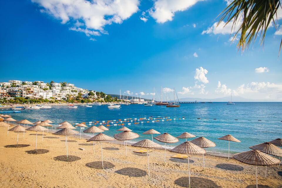 A beach with umbrellas, boats, and a coastal town.