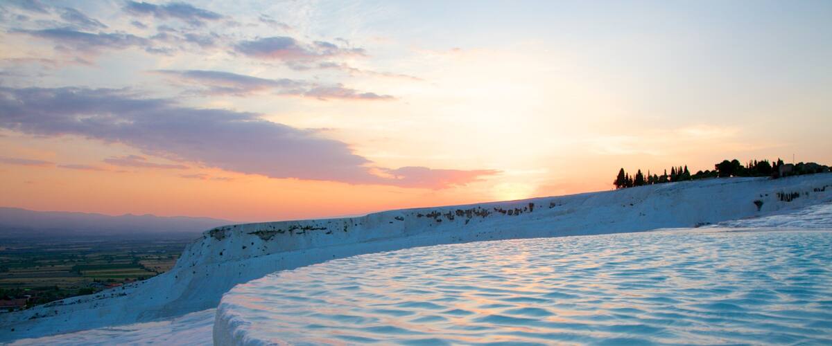 A snow-covered landscape with a curved white structure, a sunset, and a distant tree line.