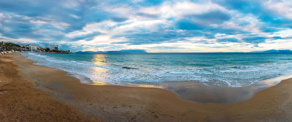 A beach with waves, a clear sky, and distant mountains.