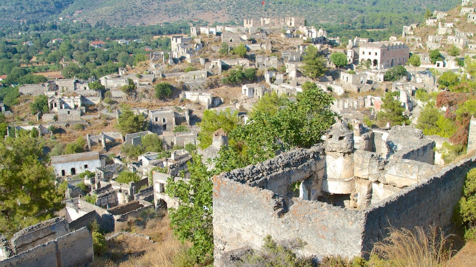 A historic town with numerous stone buildings and ruins, surrounded by greenery and hills.