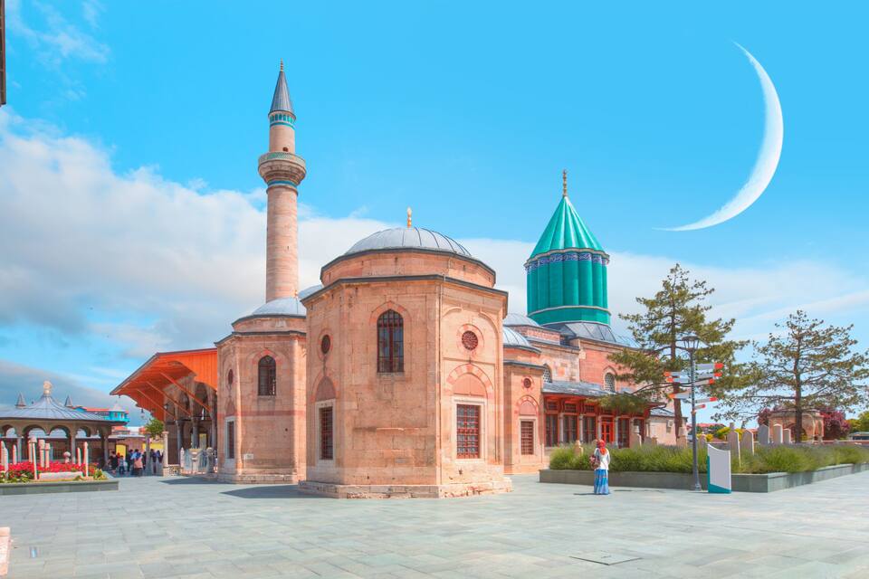 Una moschea con un minareto alto e una cupola verde, situata in una piazza con una luna crescente nel cielo.
