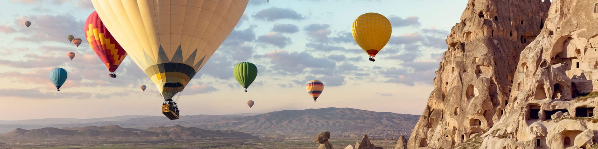 Air balloons above Turkish National Park in Goreme. Panorama of Cappadocia landscape - multi colored balloons flying over mountain valley of ancient cave town Uchisar.