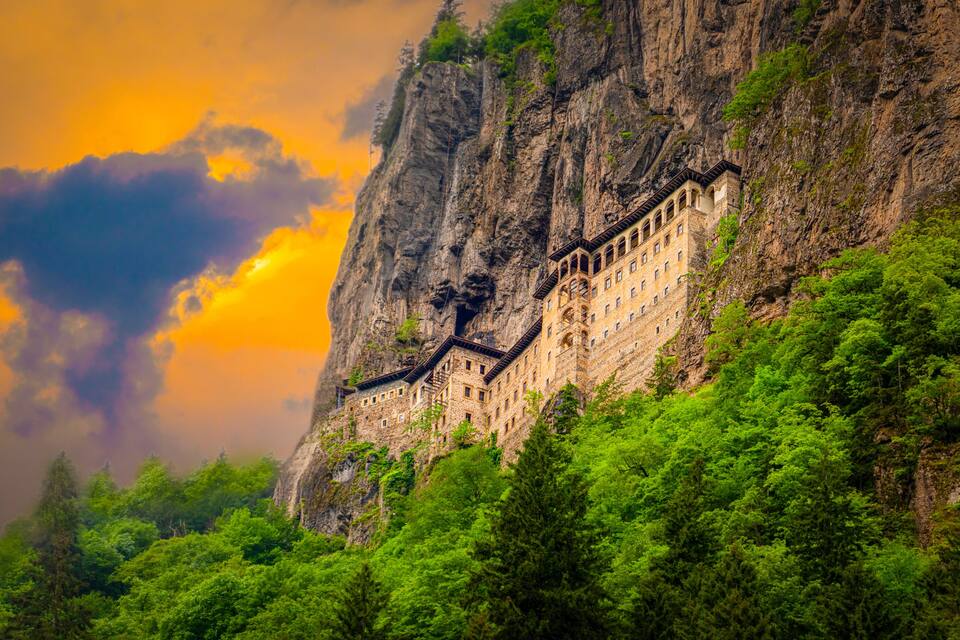 A mountain monastery with a steep cliff and lush greenery.