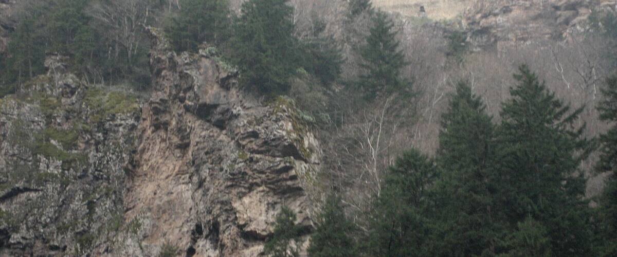A large, multi-story building with a flat roof, surrounded by rocky cliffs and dense forest.
