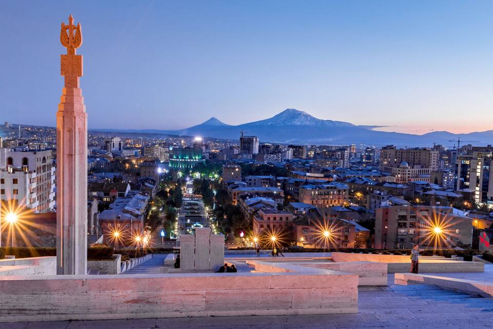 A cityscape with a prominent monument, a mountain in the background, and illuminated buildings.