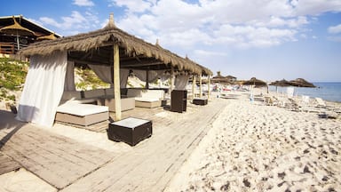 A beach with thatched-roof huts, wooden deck, and lounge chairs.