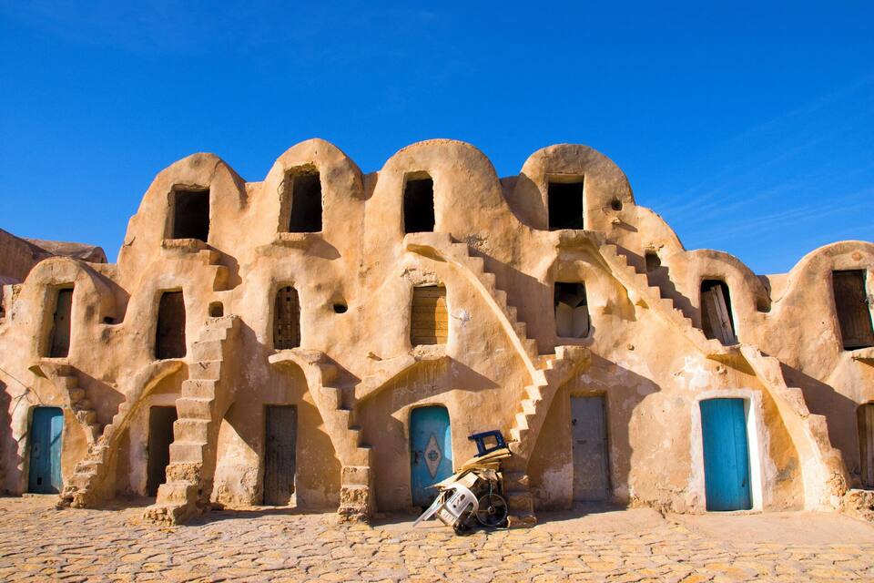 Un bâtiment historique à l’architecture unique, caractérisé par des portes en arc de cercle et une cour intérieure pavée.