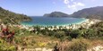 A coastal landscape with a beach, palm trees, and a mountainous backdrop.
