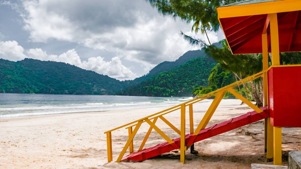 A beach with a red and yellow lifeguard tower and a staircase leading to it.