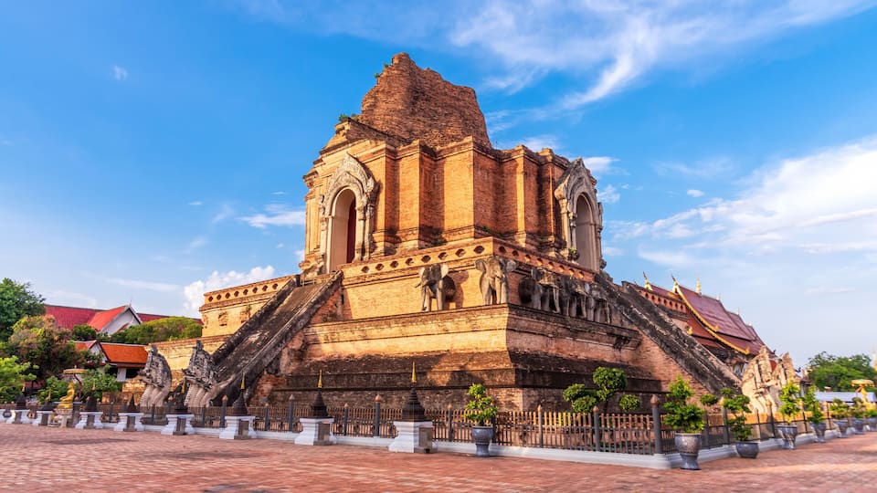 Un grand temple en briques, doté d’un escalier abrupt, entouré de plantes en pot et surplombé d’un ciel bleu clair.