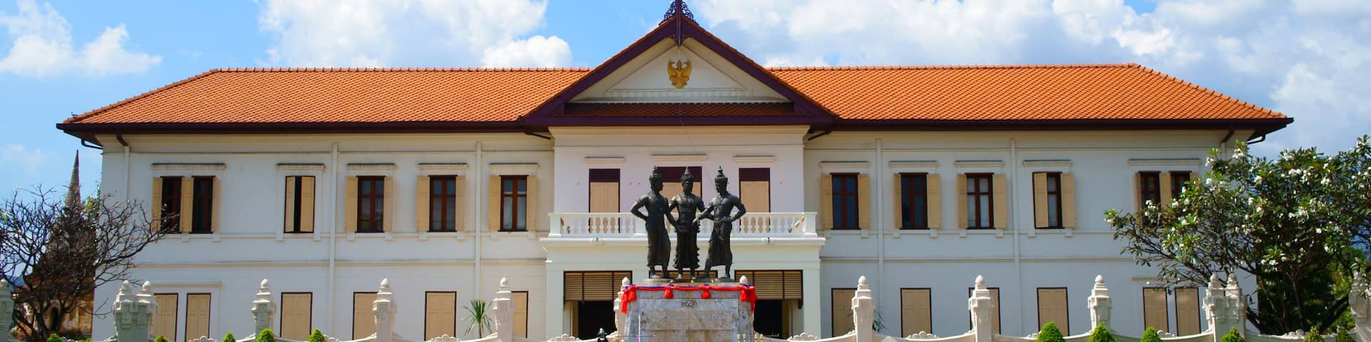 Un edificio blanco con techo rojo, una bandera y una estatua en la fachada.