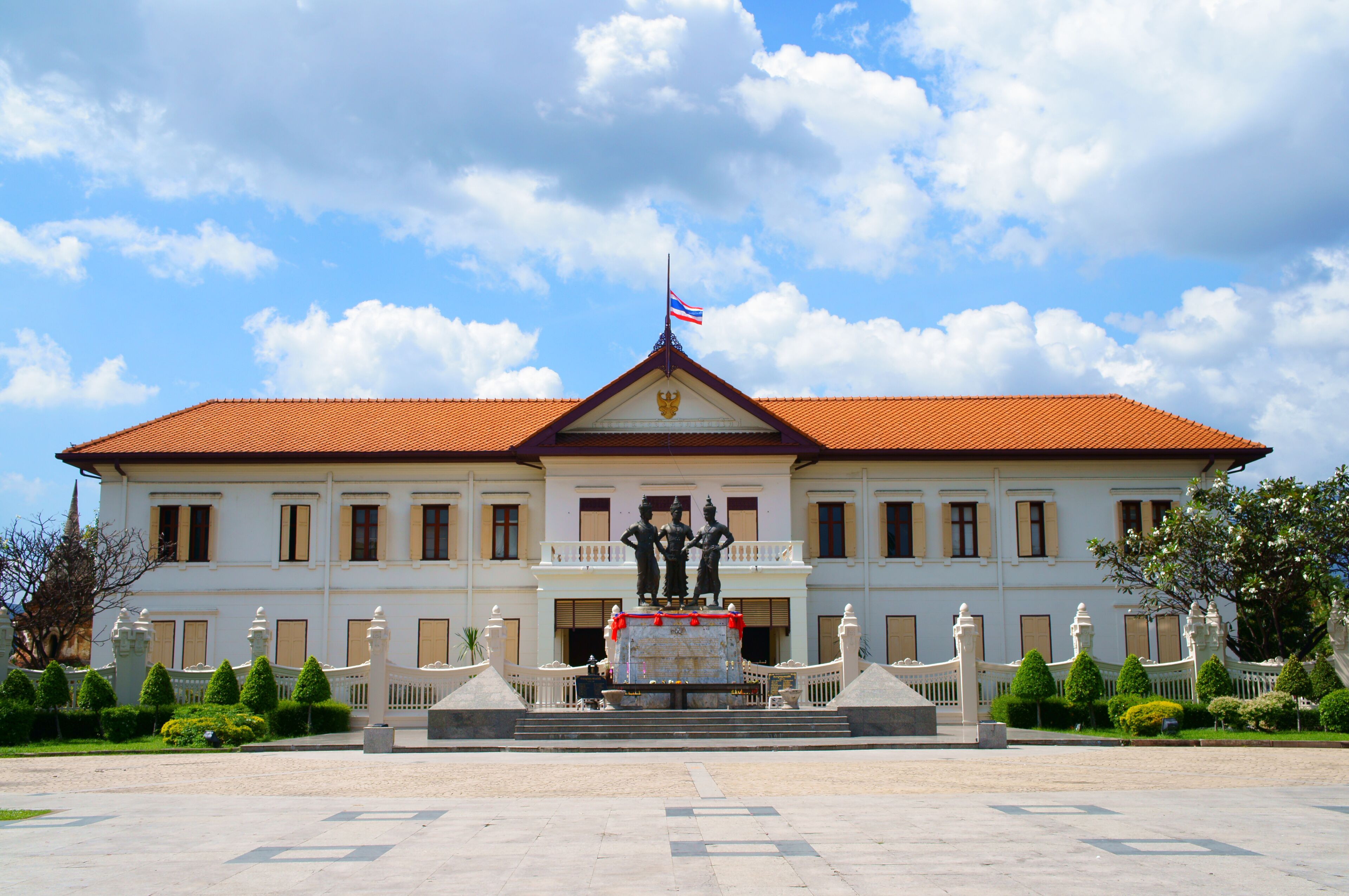 A white building with a red roof, a flag, and a statue in front.