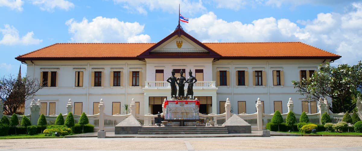 A white building with a red roof, a flag, and a statue in front.