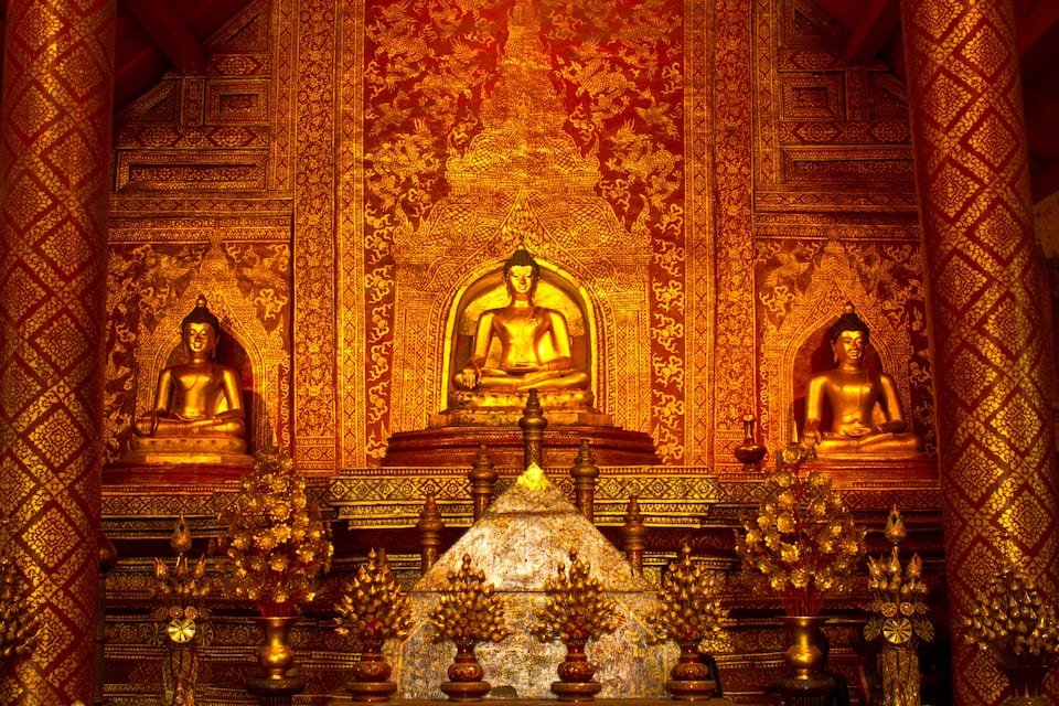 Une statue de Bouddha en or, entourée de sculptures complexes et de motifs floraux.