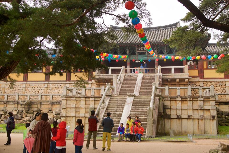 A traditional Korean building with a stone staircase leading up to it, surrounded by trees and colorful lanterns.
