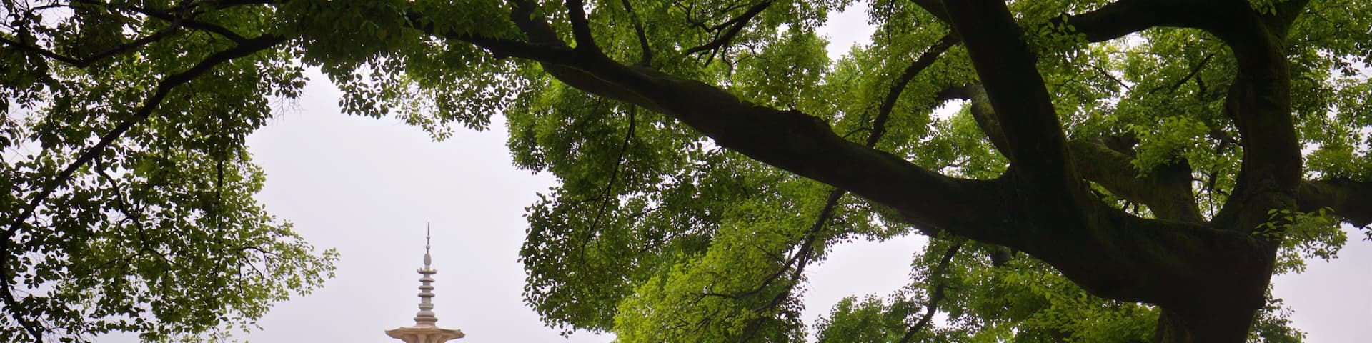 A pagoda in a park with people walking under trees.