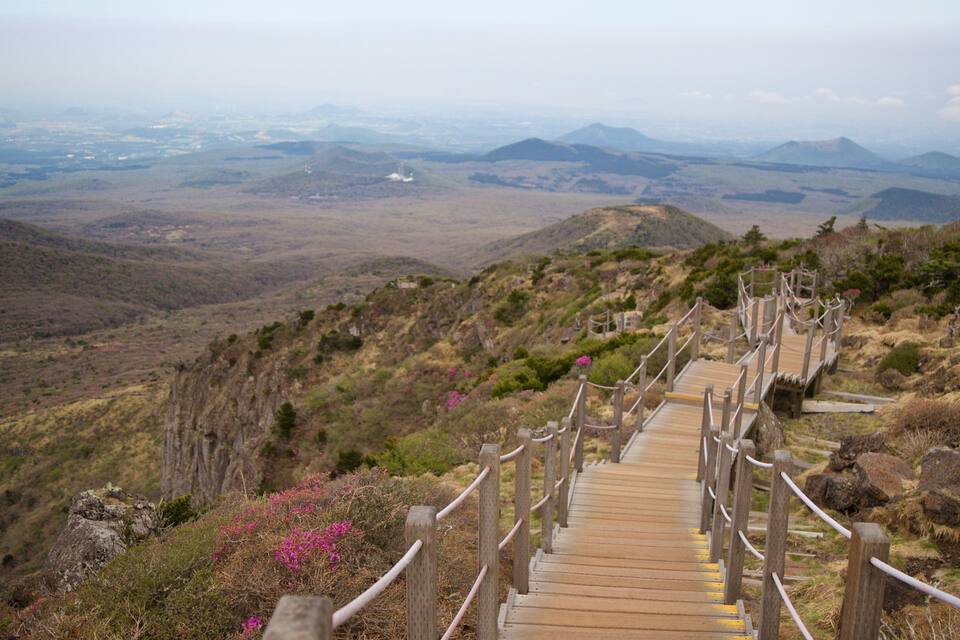 A wooden boardwalk leading through a mountainous landscape with distant views of hills and a clear sky.