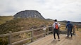 A wooden boardwalk with hikers and a mountain in the background.