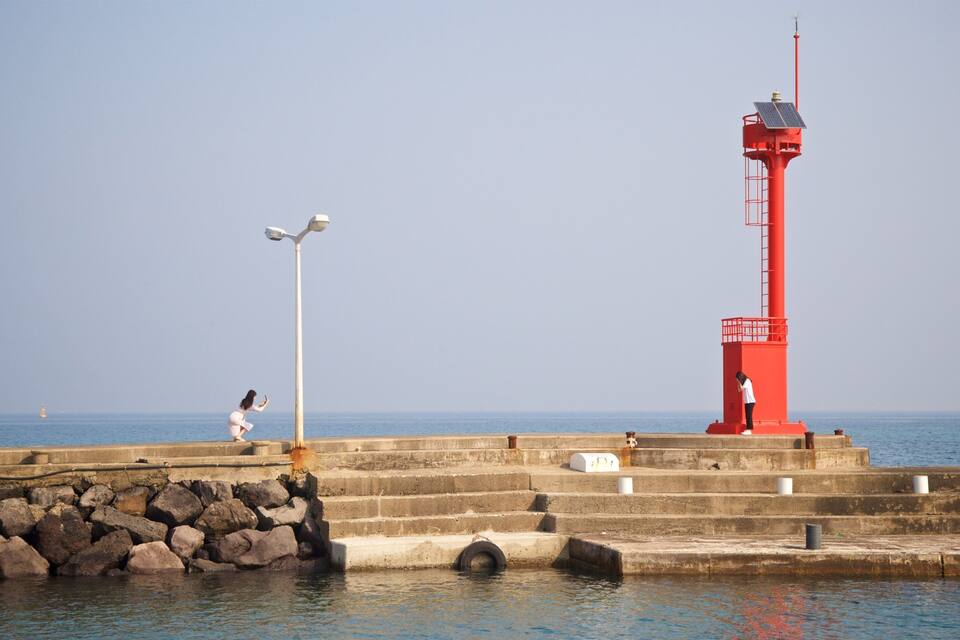 Ein roter Leuchtturm, eine Steinmole und eine Person beim Fotografieren.
