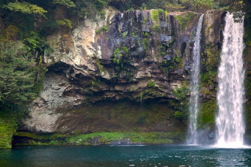 A waterfall cascading into a clear pool surrounded by lush greenery and rocky cliffs.